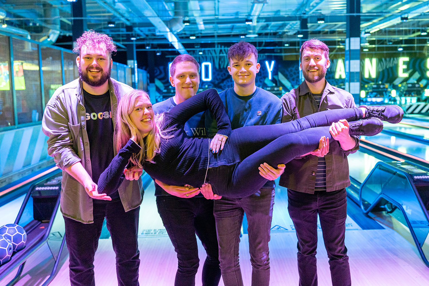 A group photo of 5 cobolt team members posing and smiling in front of a bowling alley